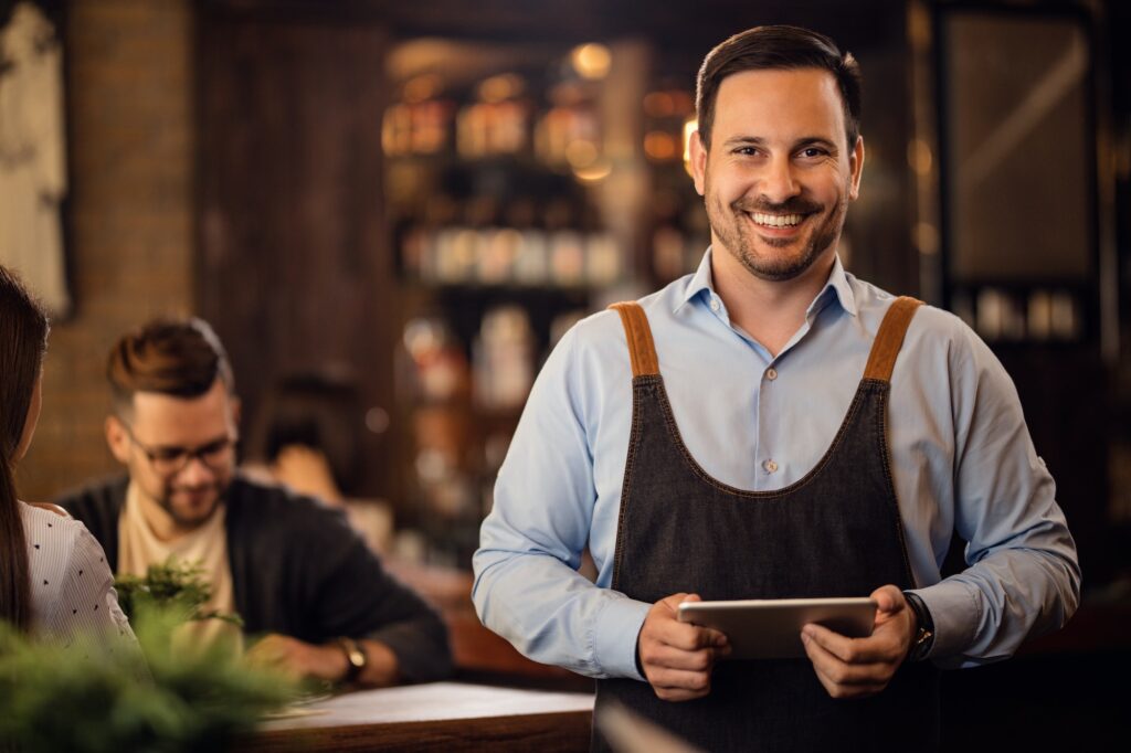 Portrait of happy waiter with touchpad in a pub.