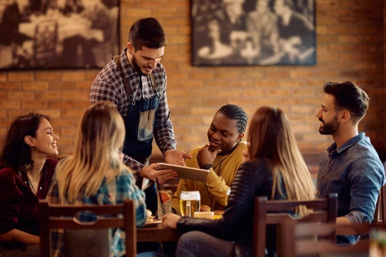 Garçom apresentando o cardápio em um tablet para clientes reunidos à mesa