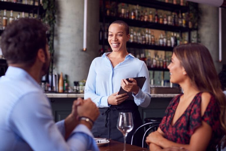 Garçonete com tablet registrando o pedido de um casal à mesa do restaurante