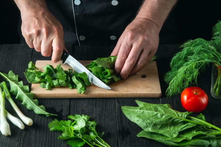 Mãos de cozinheiro cortando folhas verdes sobre uma tábua na cozinha