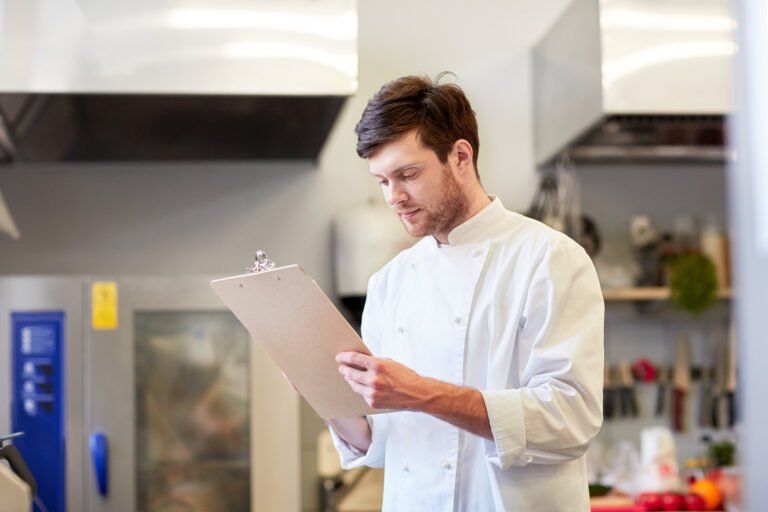 Chef registra a conferência de insumos em uma prancheta na cozinha do restaurante